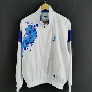 May include: White zip-up athletic jacket with blue and light blue pixelated design on the front. The jacket has blue accents on the shoulders and the text "SEGA" on the chest.