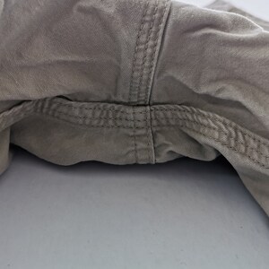 May include: Close-up of the crotch area of khaki-colored pants. The image highlights the seams and stitching details, showcasing the construction of the garment. The fabric appears to be a durable cotton blend.
