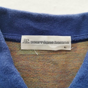 May include: Close-up of a blue polo shirt collar with a colorful patterned interior. The label reads "courr&egrave;ges homme" with a size "L". The shirt's collar is a solid blue color.