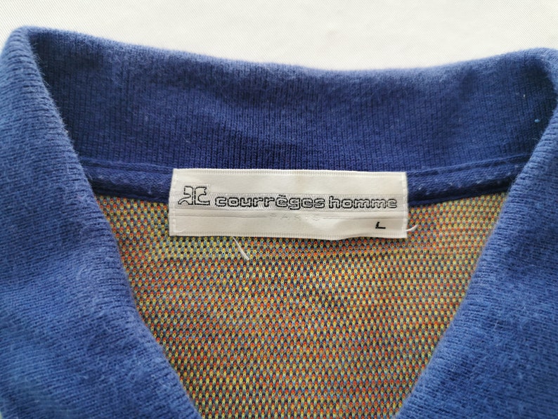 May include: Close-up of a blue polo shirt collar with a colorful patterned interior. The label reads "courr&egrave;ges homme" with a size "L". The shirt's collar is a solid blue color.
