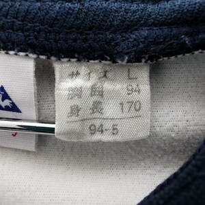 K&ouml;nnte beinhalten: Nahaufnahme eines wei&szlig;en Stoffetiketts mit japanischem Text und Gr&ouml;&szlig;enangaben. Das Etikett ist an einem wei&szlig;en Kleidungsst&uuml;ck mit marineblauem Kragen befestigt. Das Etikett enth&auml;lt die Gr&ouml;&szlig;e "L", Brustumfang "94" und H&ouml;he "170" cm.