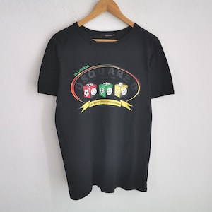 May include: Black crew neck t-shirt with a graphic print. The print features the word "DSQUARED" in an oval design with the words "IN CANADA" and "SINCE 1995". Below the oval are three colorful cube designs and a yellow banner that reads "LATEST FUNDOS DENIM CANADA".