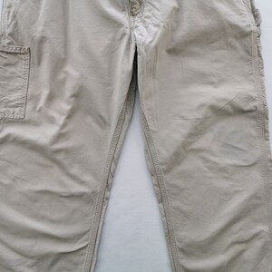 May include: Khaki-colored work pants with multiple pockets and reinforced stitching. The pants have a relaxed fit and a button and zipper closure. The fabric appears to be durable and suitable for outdoor activities.