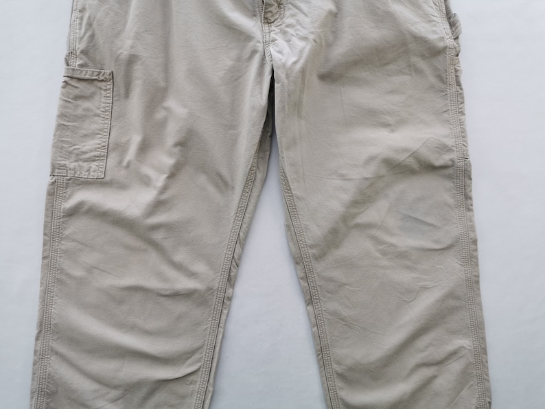 May include: Khaki-colored work pants with multiple pockets and reinforced stitching. The pants have a relaxed fit and a button and zipper closure. The fabric appears to be durable and suitable for outdoor activities.