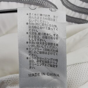 Puede incluir: Una etiqueta de tela blanca con texto japon&eacute;s y las palabras "MADE IN CHINA" en negro. La etiqueta est&aacute; adherida a una prenda blanca con una textura de malla.