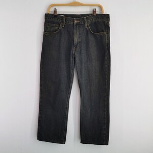 May include: Dark wash denim jeans hanging on a wooden hanger. The jeans feature a classic five-pocket design and a straight leg cut. The denim has a slightly faded appearance, with subtle colour variations.