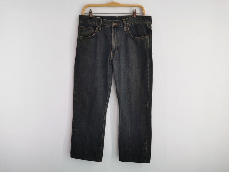 May include: Dark wash denim jeans hanging on a wooden hanger. The jeans feature a classic five-pocket design and a straight leg cut. The denim has a slightly faded appearance, with subtle colour variations.