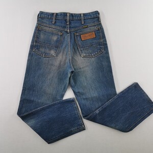 K&ouml;nnte beinhalten: Blaue Jeans aus Denim mit verwaschener Optik. Die Jeans haben ein klassisches F&uuml;nf-Taschen-Design, einen braunen Lederaufn&auml;her mit dem "Wrangler"-Logo und einen geraden Beinverlauf. Die Jeans liegen flach auf einer wei&szlig;en Oberfl&auml;che.