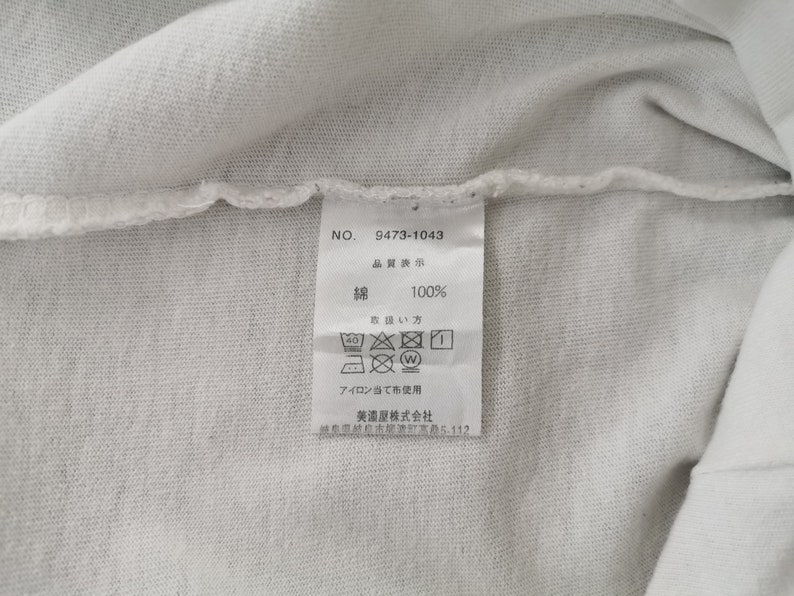 Peut inclure: Gros plan sur un tissu blanc avec une &eacute;tiquette attach&eacute;e. L'&eacute;tiquette affiche le num&eacute;ro "9473-1043" et du texte japonais indiquant que le mat&eacute;riau est 100% coton. Des instructions de lavage sont &eacute;galement affich&eacute;es.