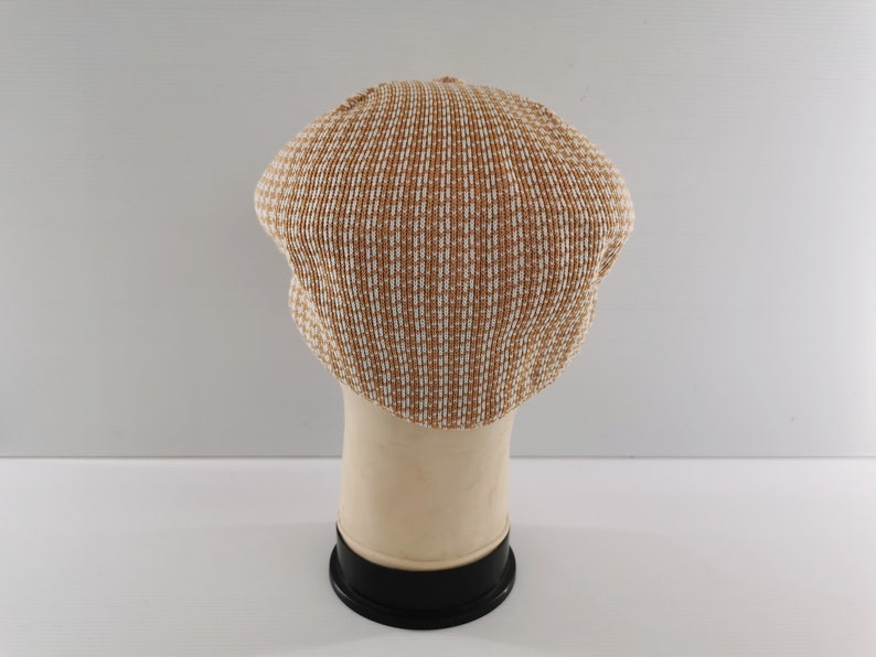 Puede incluir: Gorra de estilo newsboy con estampado marr&oacute;n y blanco. El sombrero est&aacute; hecho de un material tejido y tiene una corona redondeada y una peque&ntilde;a visera. La gorra se exhibe sobre una cabeza de maniqu&iacute; sobre un fondo blanco.