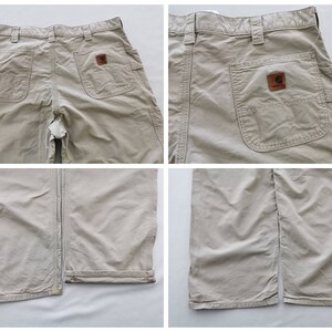 May include: Tan work pants with multiple pockets, including two large side pockets and two back pockets. A brown leather patch with the Carhartt logo is visible on the back pocket. The pants have a straight leg design.