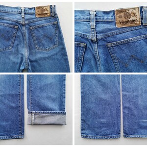 May include: Blue denim Wrangler jeans. The jeans have a classic five-pocket design, with the Wrangler logo patch on the back. The jeans are a medium wash and have a straight leg fit. The jeans are cuffed at the bottom in one of the images.