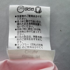 May include: A white rectangular garment care label with black Japanese text and laundry symbols. The label includes instructions to avoid machine washing, soaking, and tumble drying, and advises separating colors. The text CHINA is visible.