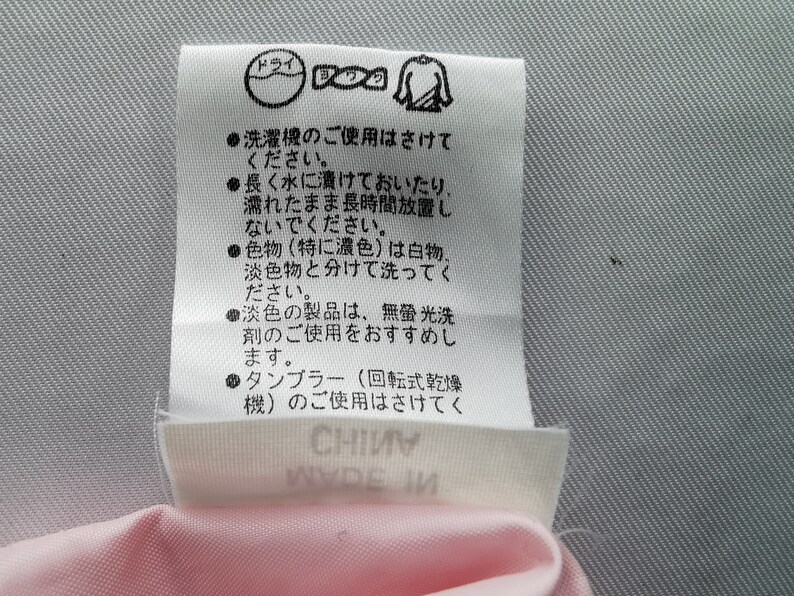 May include: A white rectangular garment care label with black Japanese text and laundry symbols. The label includes instructions to avoid machine washing, soaking, and tumble drying, and advises separating colors. The text CHINA is visible.