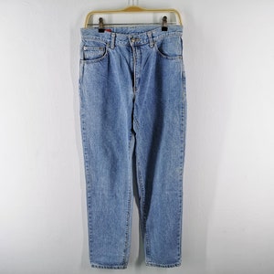 May include: Light blue denim jeans hanging on a wooden hanger. The jeans have a classic five-pocket design, a button and zipper closure, and a straight leg fit. The jeans are made of a durable denim material.