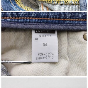 May include: Close-up of Wrangler denim jeans. The image shows the brand label, size 34, and care instructions. The jeans are made of 100% cotton.