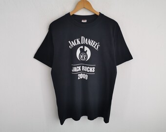Puede incluir: Una camiseta negra de manga corta con un estampado gráfico blanco. El diseño incluye el texto Jack Daniel's, un logotipo circular con Old No. 7, el texto Jack Rocks y el año 2009 impresos en blanco en el centro del pecho.