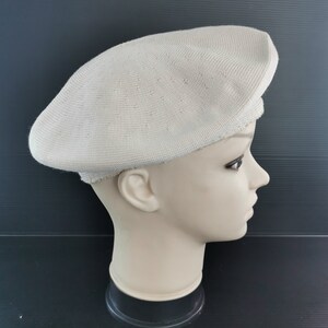 Puede incluir: Un boina beige claro con un patr&oacute;n de punto texturizado. La boina se muestra en una cabeza de maniqu&iacute; sobre un fondo oscuro. El sombrero tiene una forma cl&aacute;sica y redondeada.