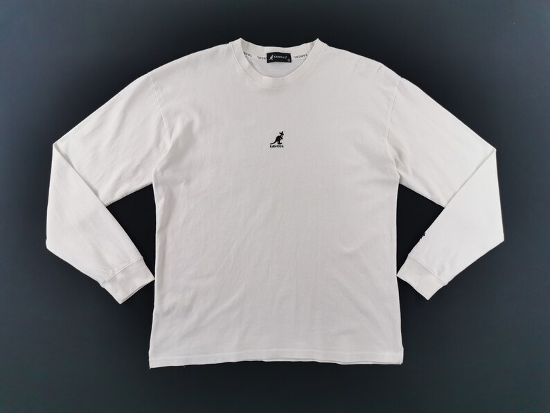 Peut inclure: Un t-shirt blanc cass&eacute; &agrave; manches longues et col rond. Le t-shirt pr&eacute;sente un petit logo kangourou noir centr&eacute; sur la poitrine et le nom de la marque imprim&eacute; sur le col. Les manches sont longues et les poignets sont c&ocirc;tel&eacute;s.