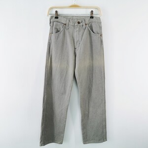 May include: Light gray denim jeans hanging on a gold-colored hanger. The jeans have a classic five-pocket design with a button and zipper closure. The pants are a straight-leg style.