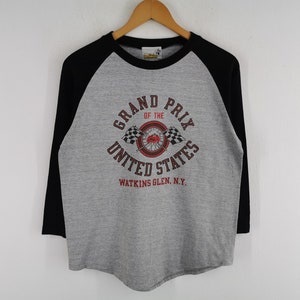 May include: A grey and black long-sleeved t-shirt with a black and white chequered flag graphic and the text "Grand Prix of the United States Watkins Glen, N.Y."