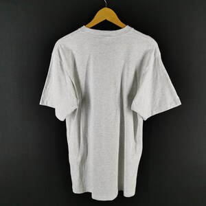 May include: A heather gray short-sleeved t-shirt hanging on a wooden hanger. The shirt is plain and has a crew neck. The background is a solid black color.