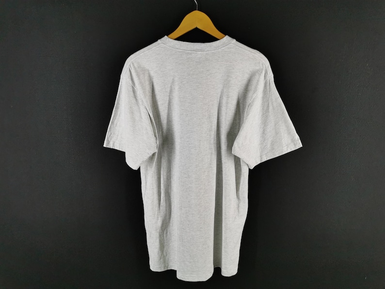 May include: A heather gray short-sleeved t-shirt hanging on a wooden hanger. The shirt is plain and has a crew neck. The background is a solid black color.