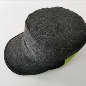 May include: A dark gray wool cap with a short brim and a flat top. The cap has a structured design with a lime green accent on the side. The hat is likely for casual wear.
