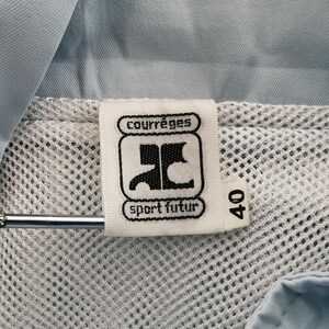 May include: Close-up of a white tag with the "courr&egrave;ges sport futur" logo and the number 40. The tag is attached to a light blue garment with a mesh lining. A silver metal object is in the image.
