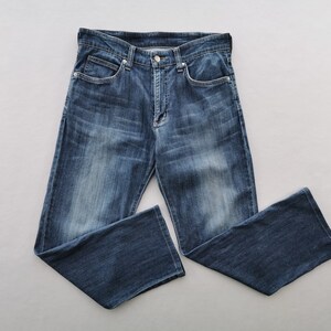 May include: Dark blue denim jeans with a classic five-pocket design. The jeans feature a button and zip fastening, belt loops, and a faded wash. The jeans are displayed flat on a grey surface.