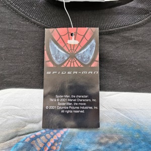 Pode incluir: Camiseta preta com etiqueta do Homem-Aranha. A etiqueta apresenta o logotipo do Homem-Aranha e o texto: "Homem-Aranha, o personagem: TM & &copy; 2001 Marvel Characters, Inc. Homem-Aranha, o filme: &copy; 2001 Columbia Pictures Industries, Inc. Todos os direitos reservados."