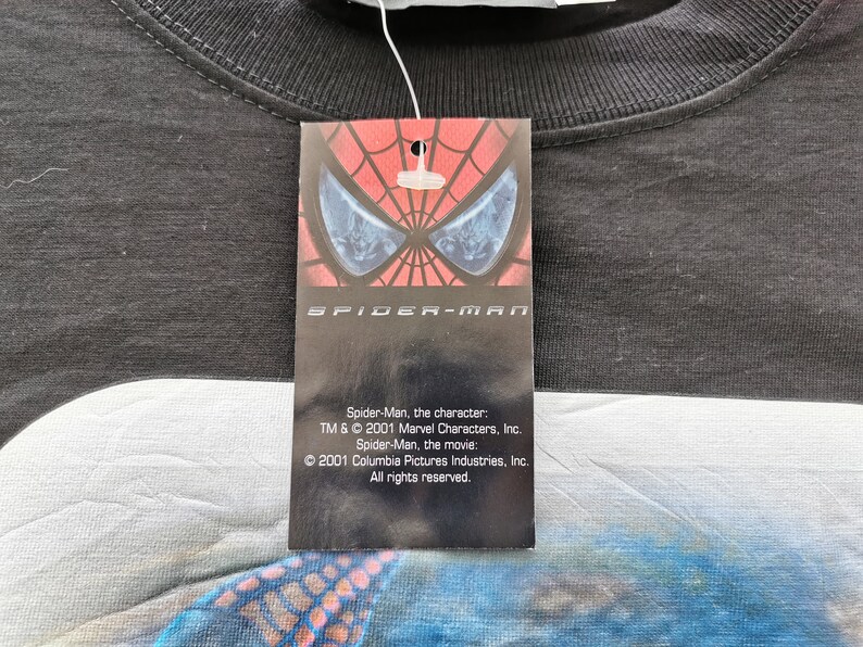Pode incluir: Camiseta preta com etiqueta do Homem-Aranha. A etiqueta apresenta o logotipo do Homem-Aranha e o texto: "Homem-Aranha, o personagem: TM & &copy; 2001 Marvel Characters, Inc. Homem-Aranha, o filme: &copy; 2001 Columbia Pictures Industries, Inc. Todos os direitos reservados."
