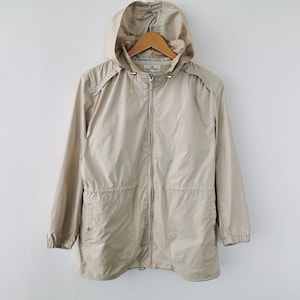 May include: A beige hooded windbreaker jacket featuring a full-length front zipper, long sleeves with elasticized cuffs, and two front pockets. The jacket includes a drawstring hood with metal toggles and a cinched waist design for a structured fit.