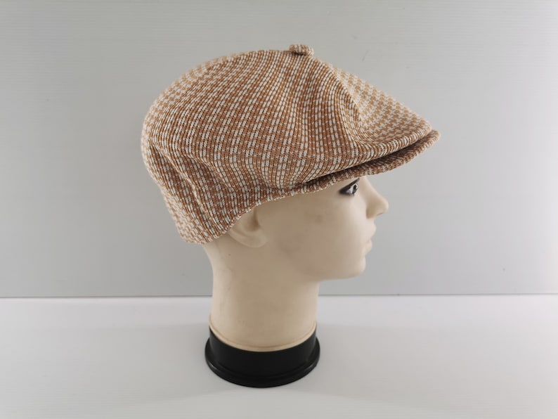 Puede incluir: Gorra de estilo newsboy con estampado marr&oacute;n y blanco. La gorra se muestra en una cabeza de maniqu&iacute;. Tiene una corona redondeada y una visera corta y r&iacute;gida. La tela tiene un aspecto texturizado.