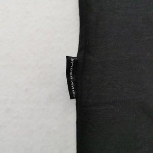 Pode incluir: Tecido preto com uma pequena etiqueta retangular anexada. A etiqueta &eacute; preta com texto branco que diz "SPIDER-MAN". O tecido &eacute; de cor preta s&oacute;lida e o fundo &eacute; branco.
