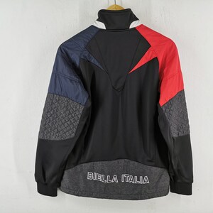 May include: A black, red, and blue athletic jacket with the text "BIELLA ITALIA" across the bottom. The jacket features a high collar and quilted gray panels on the sleeves. The design includes a red chevron on the back.