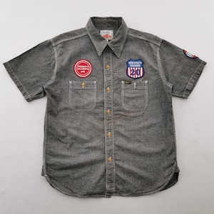 May include: A charcoal gray short-sleeve button-down shirt featuring two chest pockets and a pointed collar. The shirt is decorated with a circular red patch reading Pherrow's California Line and a shield-shaped Union & Pacific Railroad patch.