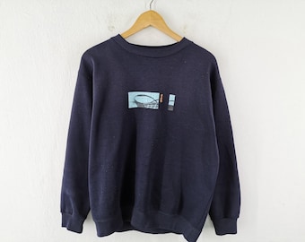Puede incluir: Una sudadera azul marino con un gráfico de una imagen azul y blanca en la parte delantera. El gráfico está en un marco rectangular con la palabra "SALO" impresa en rojo.