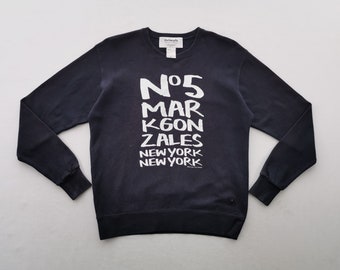 Puede incluir: Una sudadera de color azul marino oscuro de manga larga con cuello redondo y puños acanalados. El frente presenta un texto blanco serigrafiado que dice N°5 MARK GONZALES NEW YORK NEW YORK. Una etiqueta blanca es visible en el cuello.
