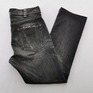 May include: A pair of black denim jeans with a faded wash. The jeans feature a classic five-pocket design, a button and zipper closure, and a leather patch on the back pocket. The back pocket has a yellow stitched "W" design.