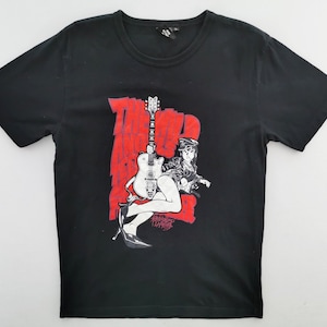 May include: Black t-shirt featuring a graphic of a woman with a guitar, set against a red backdrop. The design includes the word "BAD" in red, and the image has a vintage, comic book style.