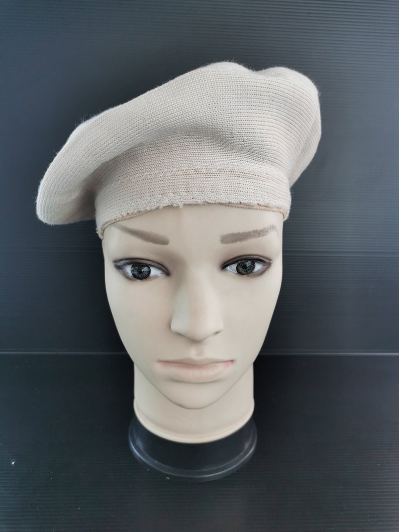 Puede incluir: Boina beige de tejido de punto acanalado. La boina se exhibe en una cabeza de maniqu&iacute;. La boina tiene forma circular y una banda alrededor de la base. La boina es de color neutro.