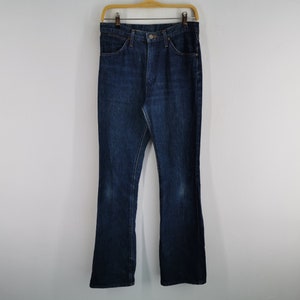 Peut inclure: Un jean en denim bleu fonc&eacute; avec une conception classique &agrave; cinq poches, suspendu &agrave; un cintre en bois. Le jean a un l&eacute;ger &eacute;vasement en bas et montre une certaine usure. Le jean est de couleur moyenne et semble vintage.
