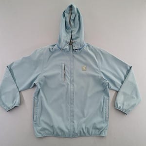 May include: A light blue hooded jacket with a zipper closure and two front pockets. The jacket has a small square emblem on the chest and a hood. The sleeves have elastic cuffs. This lightweight jacket is suitable for outdoor activities.
