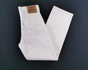 Puede incluir: Unos vaqueros de mezclilla blancos con una etiqueta de cuero color canela en la cintura trasera con el texto Levi Strauss & Co. Original Riveted Quality Clothing. Los vaqueros incluyen un bolsillo trasero con una pequeña etiqueta blanca.