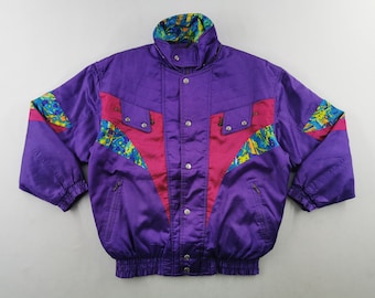 Puede incluir: Una chaqueta de invierno morada con cuello alto, mangas largas con puños elásticos y cierre frontal de cremallera con botones a presión. El diseño incluye paneles en forma de V de color rosa brillante y patrones abstractos de salpicaduras de pintura.