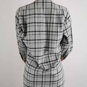 May include: A gray plaid long-sleeve shirt. The shirt features a classic plaid pattern in black and gray. The collar and cuffs have a contrasting tan and brown plaid design. The shirt is made of a soft, lightweight fabric.