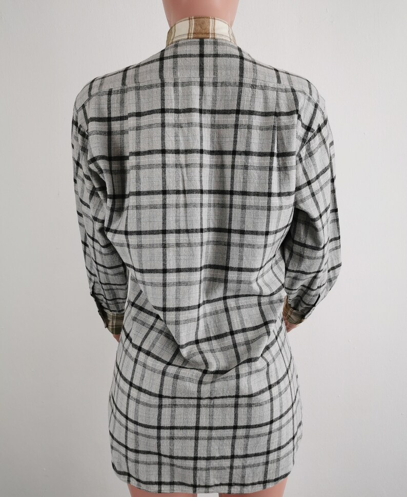 May include: A gray plaid long-sleeve shirt. The shirt features a classic plaid pattern in black and gray. The collar and cuffs have a contrasting tan and brown plaid design. The shirt is made of a soft, lightweight fabric.