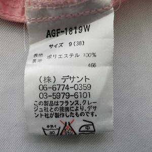 May include: A white fabric clothing care label with black text, featuring the code AGF-1819W, size 9 (38), and 100% polyester composition. It includes Japanese text, contact phone numbers, and three laundry instruction symbols at the bottom.