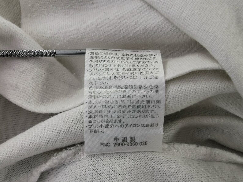 Peut inclure: Gros plan sur un tissu blanc avec une &eacute;tiquette cousue. L'&eacute;tiquette contient du texte japonais et le num&eacute;ro "2600-2360-025". Le tissu est l&eacute;g&egrave;rement froiss&eacute;.
